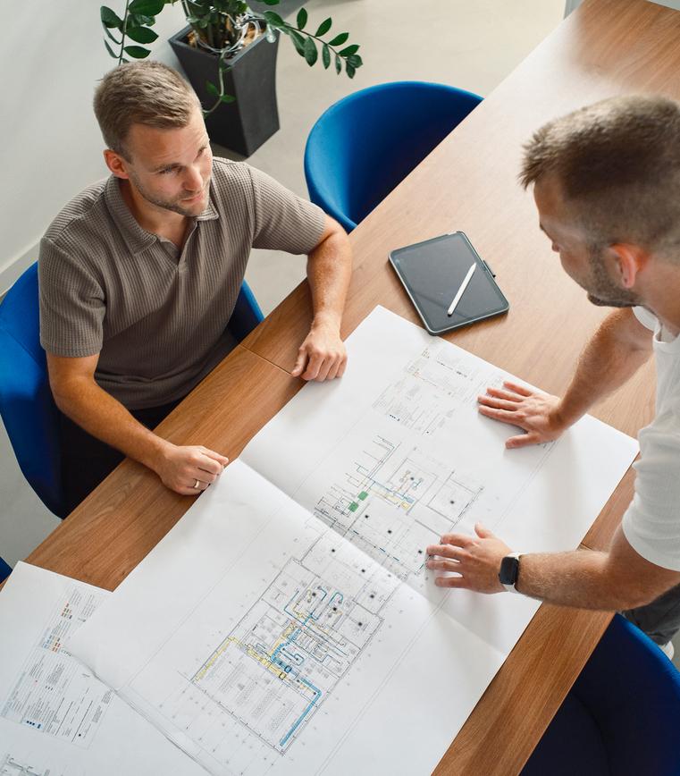 Zwei Männer stehen über Bauplänen an einem Tisch und besprechen Details.