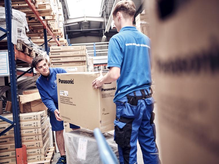 Zwei Northoff-Mitarbeiter tragen einen großen Panasonic Karton in einem Lagerraum.