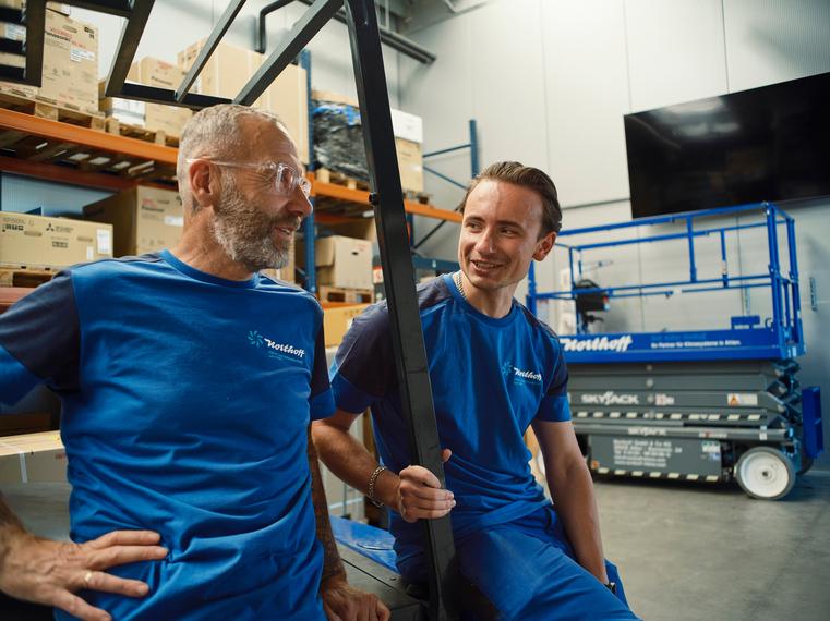 Zwei Northoff-Mitarbeiter in blauen Shirts unterhalten sich lächelnd im Lager.