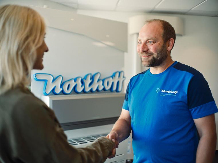 Ein Northoff-Mitarbeiter schüttelt einer Kundin an einem Empfangstresen die Hand.