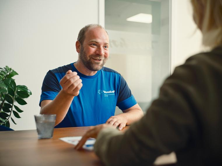 Ein lächelnder Northoff-Mitarbeiter im Gespräch mit einer Kundin am Tisch.