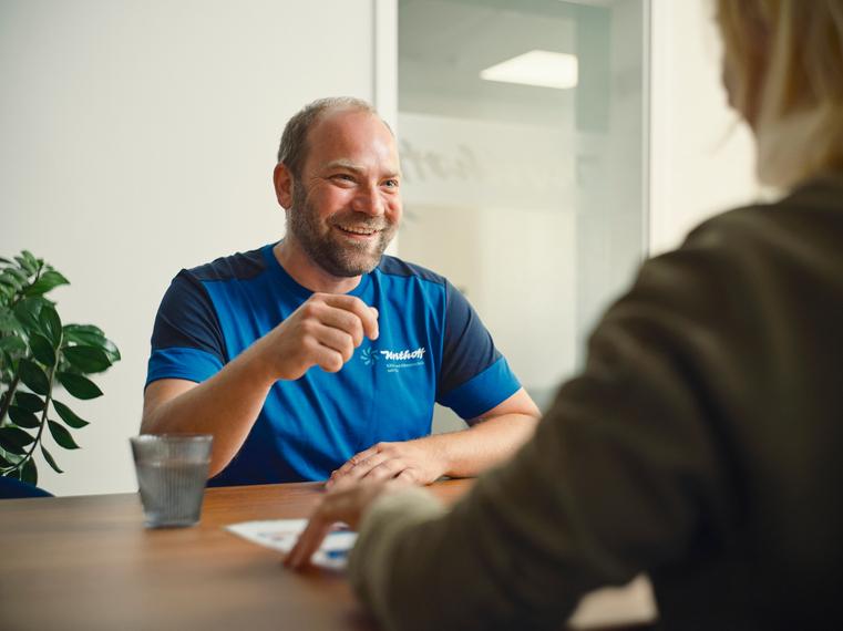 Ein lächelnder Northoff-Mitarbeiter im Gespräch mit einer Kundin am Tisch.