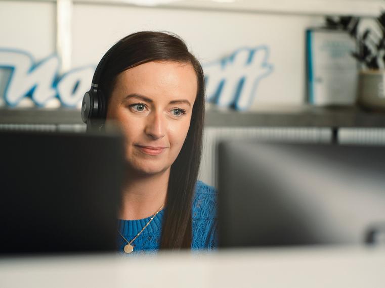 Eine Northoff-Mitarbeiterin mit Headset arbeitet konzentriert an einem Computerbildschirm.