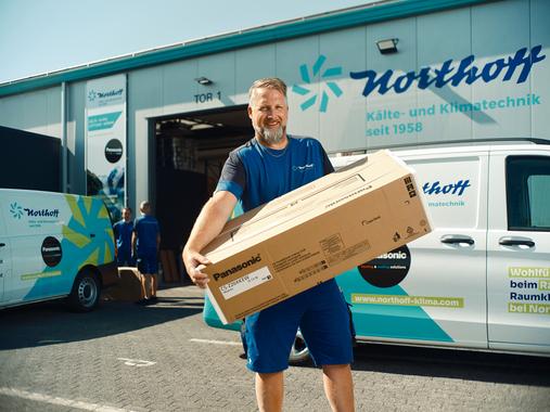Ein Northoff-Mitarbeiter trägt einen großen Panasonic Karton vor dem Lagergebäude.