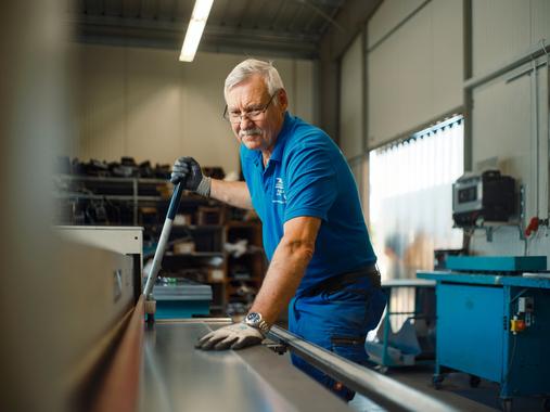 Ein älterer Northoff-Mitarbeiter in blauer Arbeitskleidung arbeitet an einer Metallbearbeitungsmaschine.