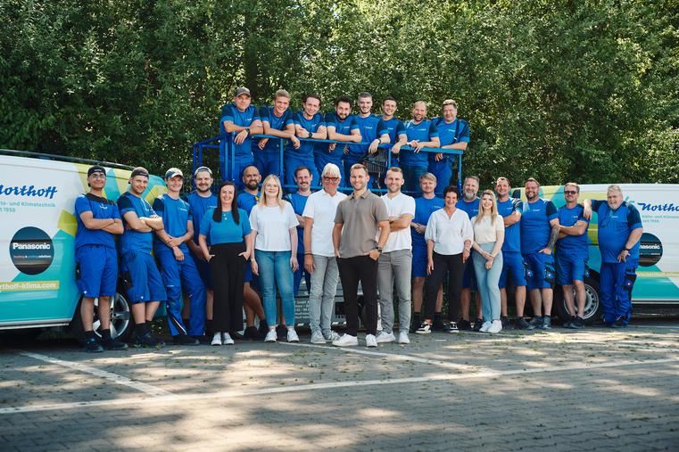 Großes Northoff Teamfoto mit vielen Mitarbeitern in blauer Kleidung vor Firmenvans.