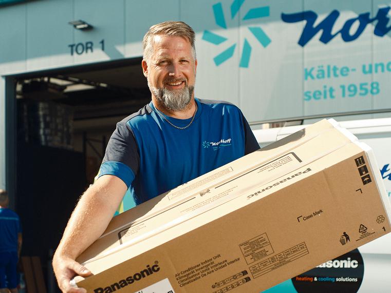 Ein Northoff-Mitarbeiter trägt einen großen Panasonic Karton vor dem Lagergebäude.