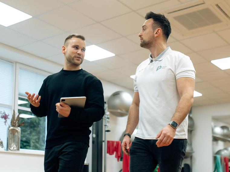 Zwei Männer, einer mit Tablet, besprechen sich in einem Fitnessstudio.