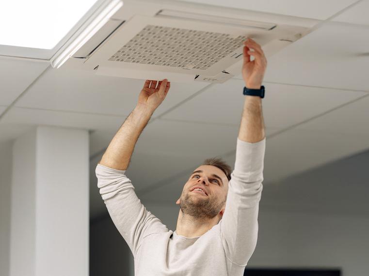 Techniker installiert oder wartet eine Deckenklimaanlage oder Lüftungseinheit in einem Innenraum.
