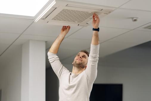 Techniker installiert oder wartet eine Deckenklimaanlage oder Lüftungseinheit in einem Innenraum.