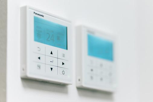 Nahaufnahme eines digitalen Panasonic Thermostats an der Wand, zeigt Raumtemperatur 24°C.