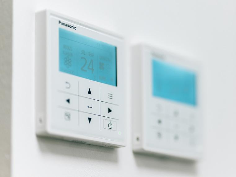 Nahaufnahme eines digitalen Panasonic Thermostats an der Wand, zeigt Raumtemperatur 24°C.