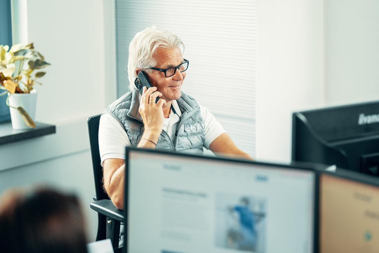 Mann am Schreibtisch telefoniert vor Computermonitoren. Repräsentiert Beratung für Klimaanlagen und Service