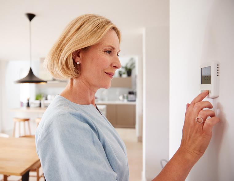 Frau stellt digitales Thermostat an der Wand ein. Klimatisierung und Raumklimasteuerung im Privathaushalt.
