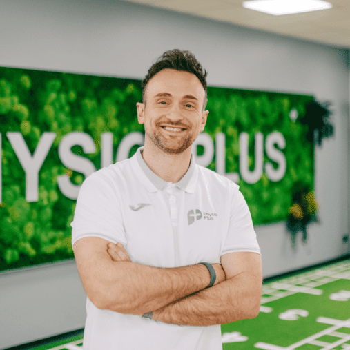 Trainer lächelt in Physiotherapie-Praxis mit Kunstrasen. Stellt Klimasysteme und Lüftungstechnik für Sportstätten dar.