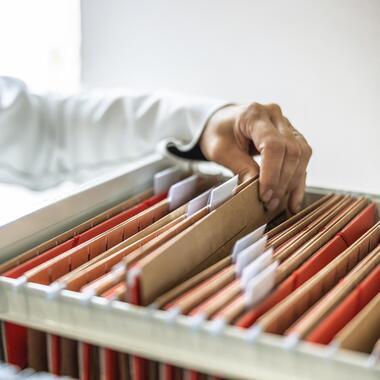 Hand greift in Aktenschrank mit Hängeregistern. Repräsentiert Klimatisierungslösungen für Büros und Verwaltung.