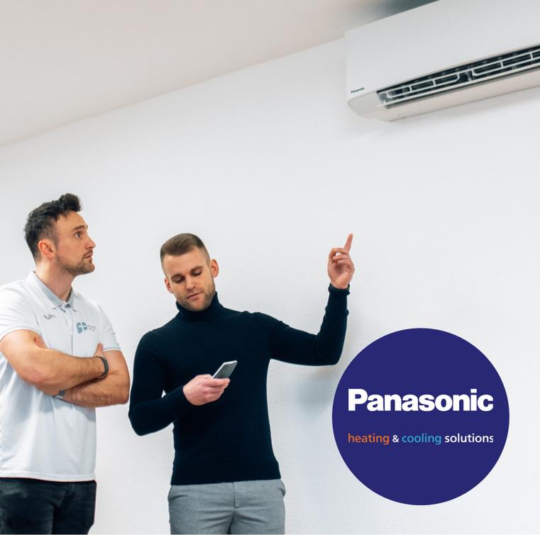 Zwei Männer betrachten eine Panasonic Wandklimaanlage, einer zeigt darauf.