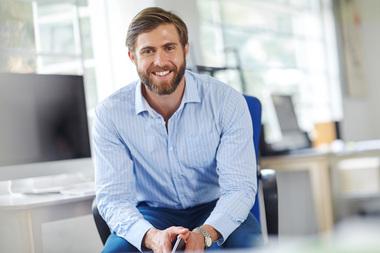 Lächelnder Geschäftsmann in Hemd sitzt im modernen Büro. Symbolisiert Klimasysteme für gewerbliche Büroräume.