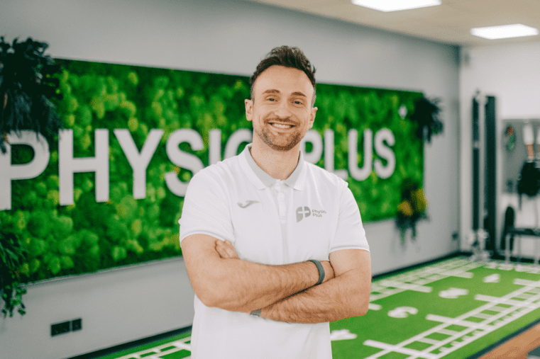 Trainer lächelt in Physiotherapie-Praxis mit Kunstrasen. Stellt Klimasysteme und Lüftungstechnik für Sportstätten dar.