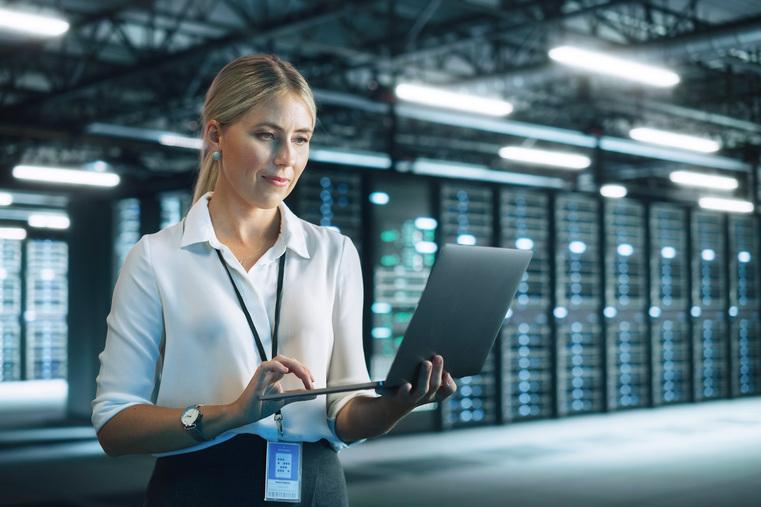 Frau nutzt Laptop in Serverraum mit leuchtenden Racks. Symbolisiert Präzisionsklimatisierung für Rechenzentren.