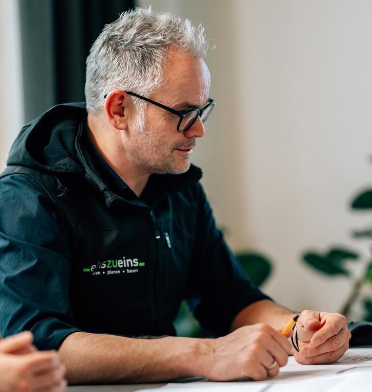 Mann mit Brille in dunkler Jacke blickt auf Dokumente am Tisch, im Kontext der Klimatisierungs-Planung.